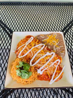 Plato de enchiladas de pollo servido con frijoles arroz y crema