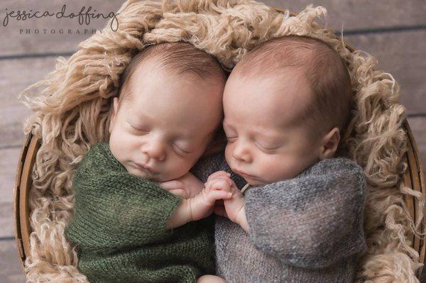 Newborn twin brothers holding hands.