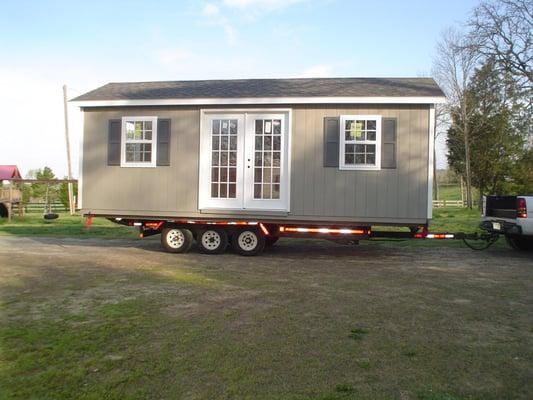 Dove grey and white trim shed with black architectural shingles.  Has metal house doors, garage door and vinyl shutters that ...