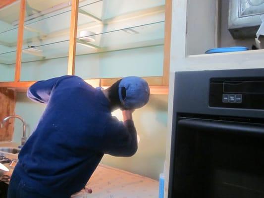 Completing installation of glass shelves and glass backslash in kitchen.