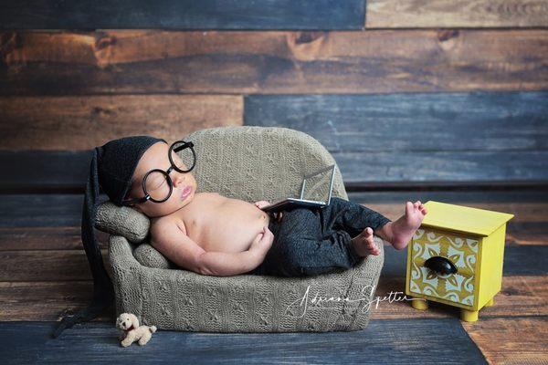 Newborn photo session with baby sleeping on couch with a laptop and glasses.