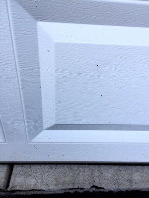 Tar splatter spots on bottom panel of white garage door.