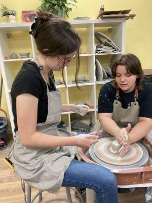 Instructor Alexis teaching a beginner how to center on the pottery wheel.