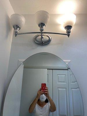 Light fixture is hung upside down, off-center & too low to flip around. Mirror is round, but mounted on a visible square box.