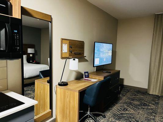 Desk, mirror, and TV area next to kitchenette.