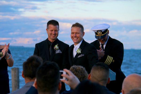 Two grooms standing close to each other and smiling because they just got married.