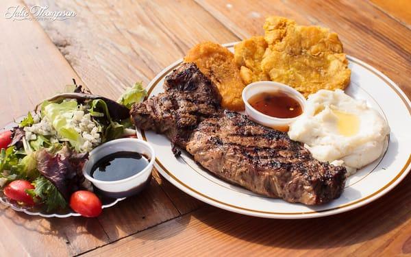 Rib-eye steak meal with plantains, mashed potatoes and side salad. ©@julieimagery