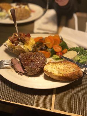 Filet mignon with garlic butter, loaded baked potato, toasted bread and vegetables.