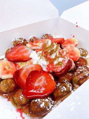 Vanilla Bubble Waffle with strawberry drizzle, fresh strawberries, bananas, whip, cinnamon, maple syrup and powdered sugar