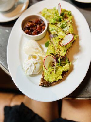 Avocado toast with poached eggs and bacon on the side.