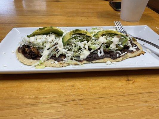 Huarache with barbacoa de chivo. Has black beans, nopales (cactus), cabbage, lettuce, avocado and cheese.