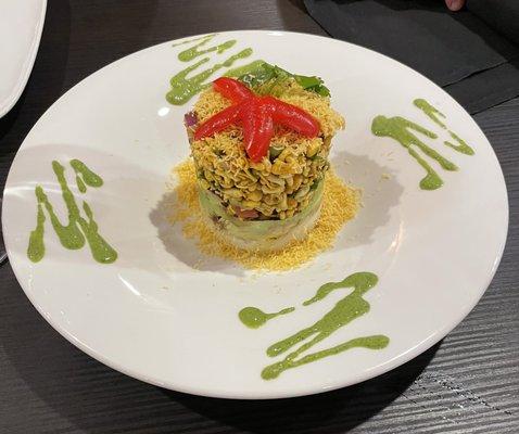 AVOCADO JHALMOORI - Rice puffs and avocado layered with a mix of onion, tomato, mint, and tamarind sauce served with banana chips