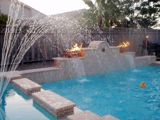 Pool and spa with elevated walls, fountain, and fire bowl accents.