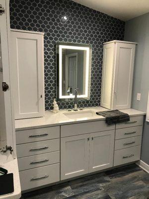 Charming bathroom vanity with extra storage featuring sleek white cabinetry and elegant hardware designed by Apollo Kitchen & Bath.