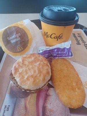 Coffee, hash brown, and sausage biscuit with grape jelly