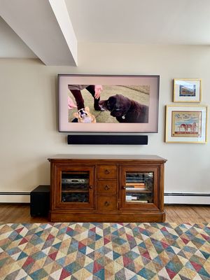 65" Samsung TV in ambient Art mode displaying artwork with definitive technology sound bar below