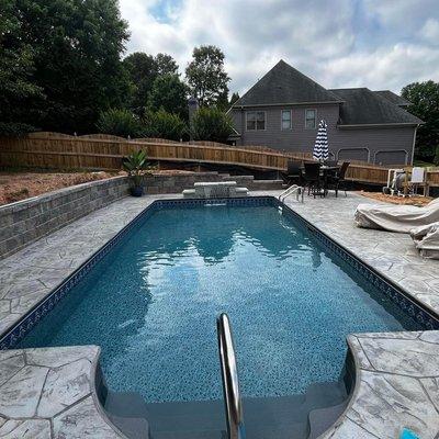 In ground vinyl liner pool with stamped, colored and sealed concrete, sheer descent waterfall and a diamond pro retaining wall.