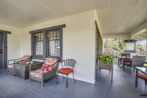 Front of craftsman-style property's front porch with two sets of wicker chairs and glass tables. Wicker armchairs and coffee table.