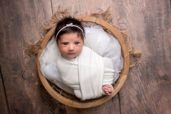 baby girl wrapped in white in a bowl prop with a pearl layer during her newborn session