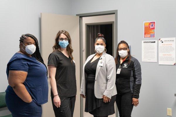 Four women stand in a waiting room wearing surgical masks