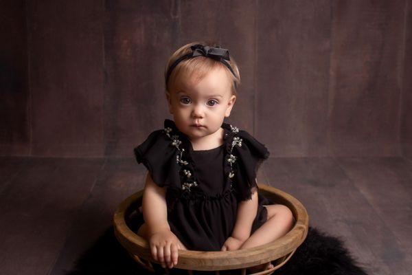 baby girl in a custom black outfit, sitting a wooden bowl prop during her cake smash session