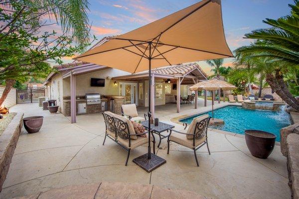 Spacious backyard patio area with seating, pool and spa, and built in outdoor kitchen with grill and refrigerator.