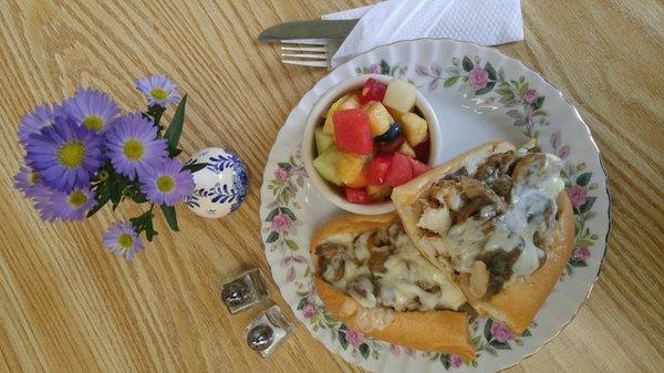 Cheesesteak and fresh cut up fruit.