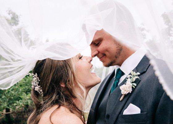 a newly married couple under her veil smiling.