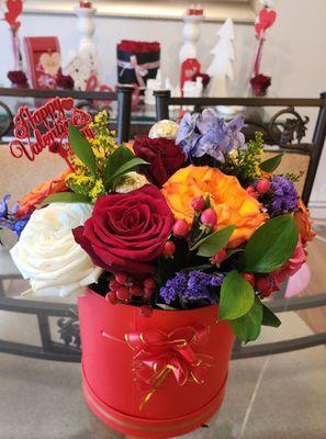 A beautiful red box adorned with a lavish gamut of roses and an array of colors that renders the arrangement...