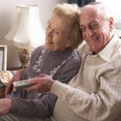 The clients are enjoying watching tv while the caregiver is doing light housekeeping. She giving them some alone time.