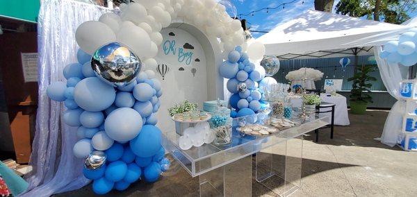 Dessert acrylic table set up with white arch, balloon garland and some treats.