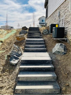 Custom built stair case using concrete step units with large boulders & outdoor lighting for enhanced landscape appeal.