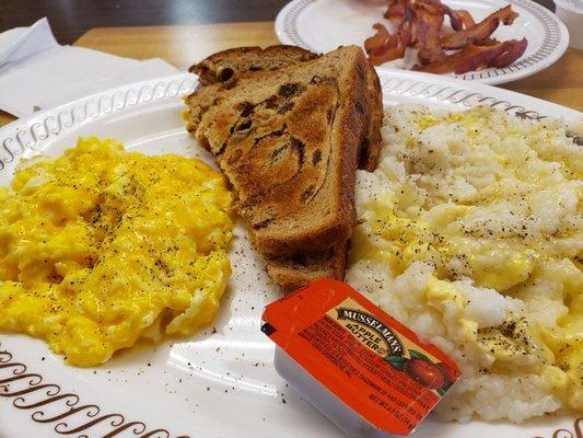 Cheesy eggs, Cinnamon raisin toast, and grits with a side of bacon.