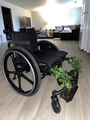 a custom wheelchair. it is completely black and has handle bars, a medium-height backrest, side guards and armrests.