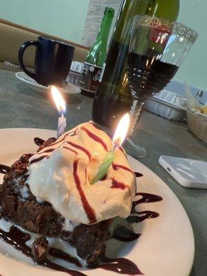 Chocolate brownie with vanilla ice cream and caramel and chocolate syrup accompanied with some red wine.