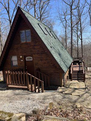 A-frame Cabin 6 front view with charcoal grill and woods backdrop.