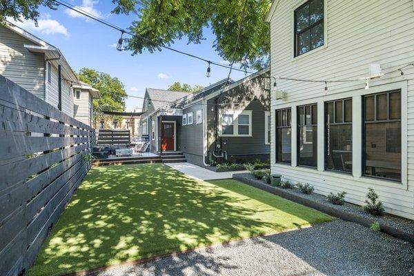 backyard artificial grass with horizontal fence, gravel walkway, hanging lights and some low mentainance planting