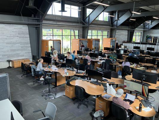 Open space equipped with adjustable desks, massive HD displays, and phonebooths.