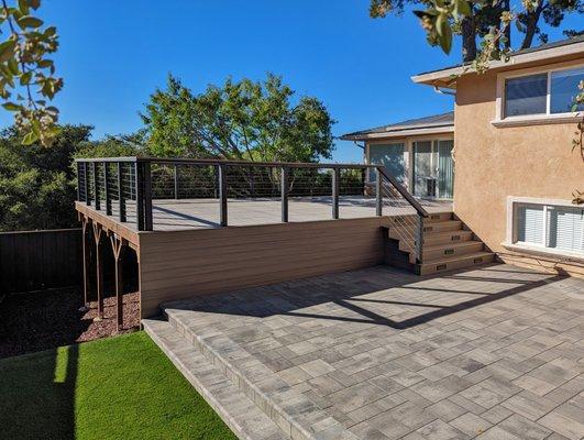 Composite deck with cable railing and and step lights. Pavers and bullnose coping. Artificial turf. Mulch.