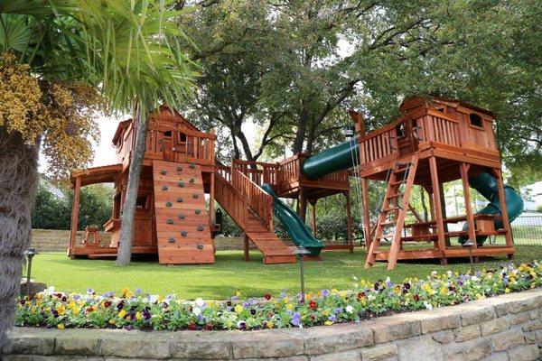 Fort Stockton playsets bridged to tree deck with swings, slides, and cabins.