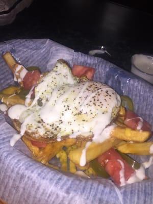 Garbage fries. Basket of fries loaded with cheddar cheese jalapeños and tomatoes, topped with a fried egg with a ranch drizzle