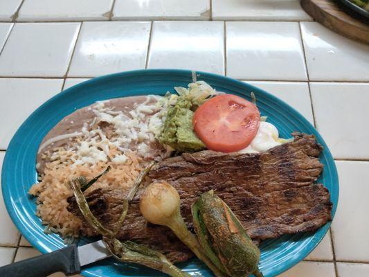 Carne Azada. Grilled steak served with rice, beans, lettuce, sour cream, guacamole. Top with a grill jalapeno and grill onions.