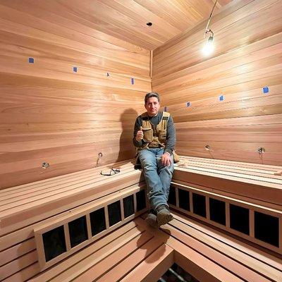 Professional carpenter proudly displaying his craftsmanship inside a newly constructed wooden sauna.