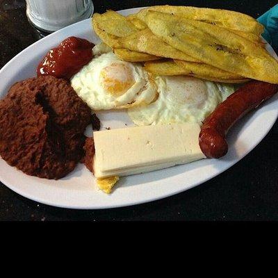 Un Desayuno que trae Tajadas de platano, Uevos, Frijoles Fritos, Queso Crema con un HotDog Frito