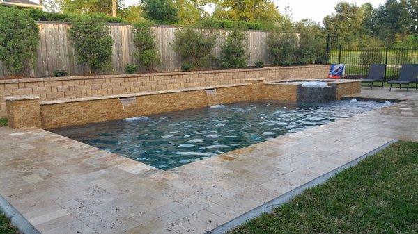 Pool and spa with raised wall water fall. All travertine. Retention wall with landscape.