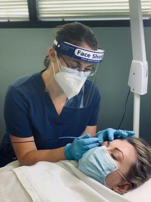 Courtney performing electrolysis permanent hair removal while keeping her patient/personal protective equipment on.