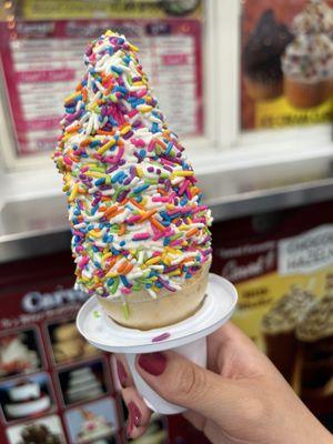 Vanilla soft serve with rainbow sprinkles in a cone