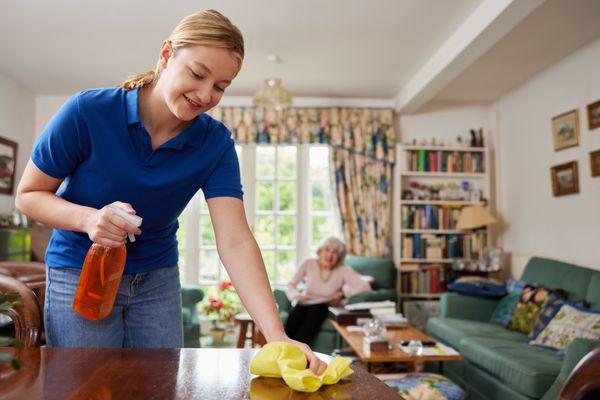 Companion homemaker helping clean around home and talking to senior woman.