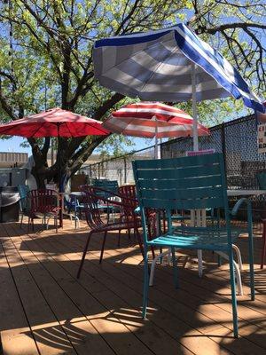 Shady patio with wooden picnic benches and metal lawn furniture.