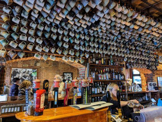 Inside. Bar with a bunch of beer mugs on the upper wall and ceiling.